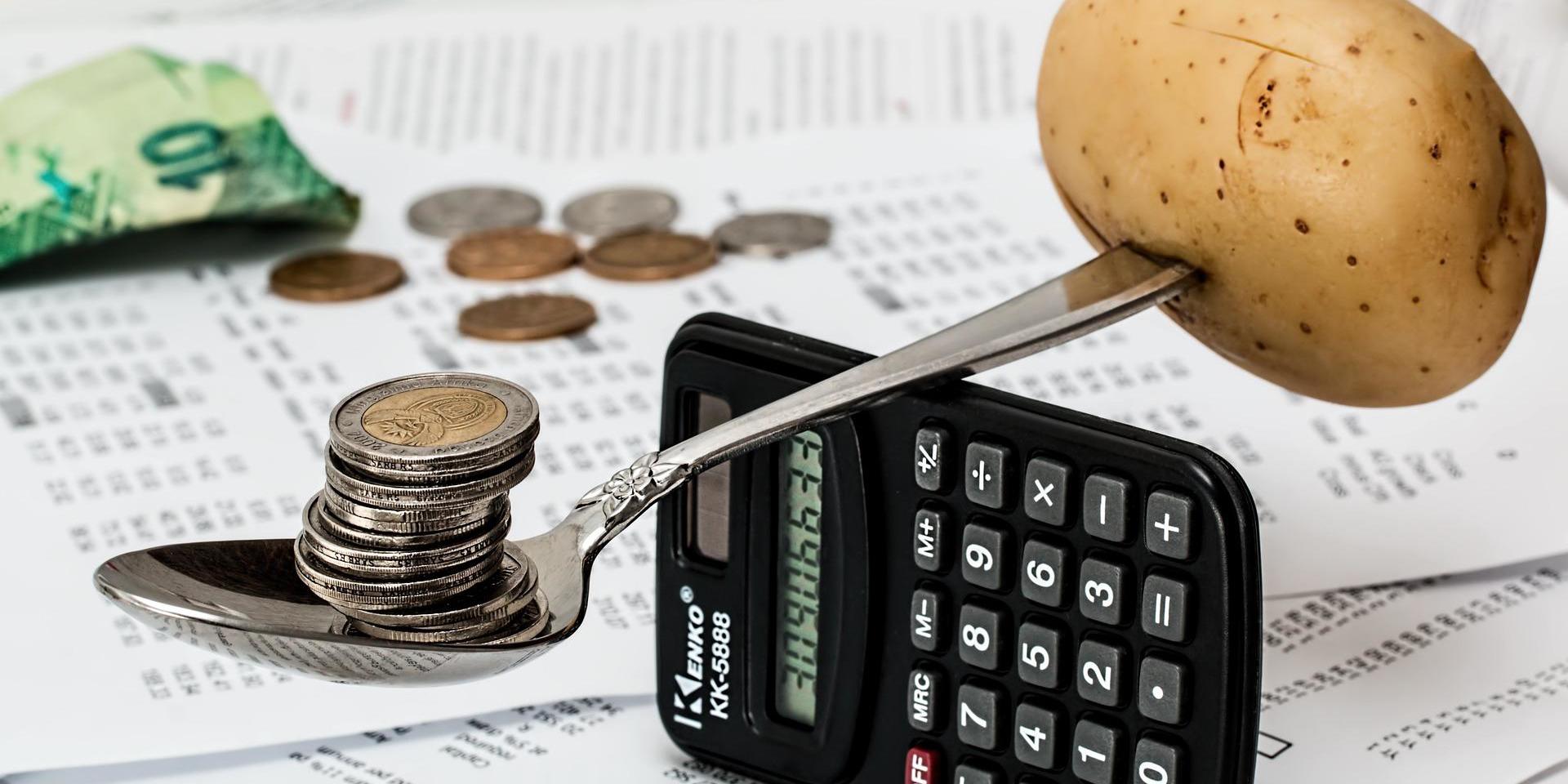 A spoon balancing a potato and some coins, on a calculator